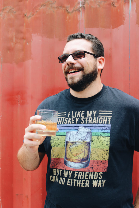 A man enjoying a glass of bourbon while wearing a shirt that reads "I like my whiskey straight, but my friends can go either way."